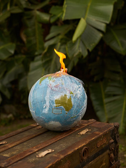 Image of a globe with a fire lit on it as if it were a bomb, a clever way to remind people to take care of our environment because the earth's health is like a ticking time bomb about to explode if we don't take good care of it, shown on BibBoutique.com